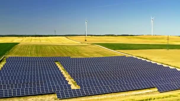 Потрясающие солнечные батареи на поле в летнее время и ветряные турбины на заднем плане, вид с воздуха, Польша — стоковое видео