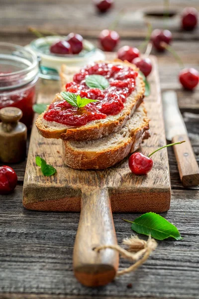 Sanduíche saboroso com geléia feita de cerejas na mesa de madeira — Fotografia de Stock