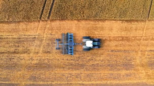 収穫後の畑を耕す青いトラクターの空中風景 — ストック動画