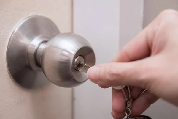 Close up of woman's hand using key for unlocking or locking the white door