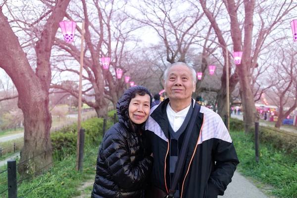 Sakura bahçesinde seyahat sırasında gülümseyen yaşlı bir Asyalı Çift, Japonya. Emeklilik yaşam tarzı kavramı