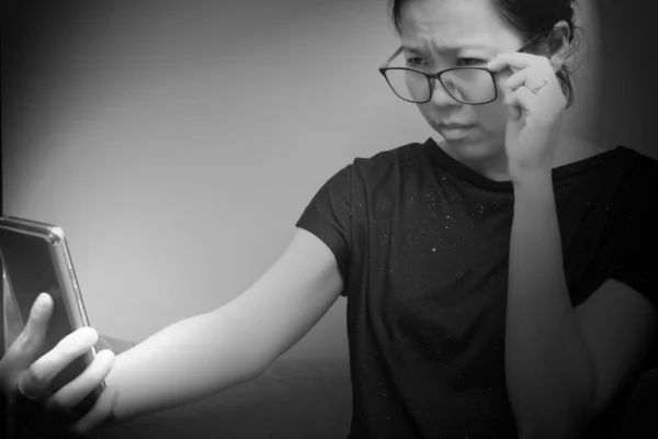 Asian female trying to read something in her mobile phone. poor sight, farsightedness, myopia. Black and white tone