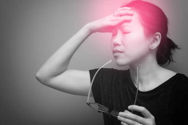 Asian woman holding glasses, suffer from having a strong headache and fever, poor sight, farsightedness, myopia. black & white tone with red spot on her head