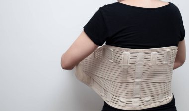 Siyah tişörtlü kadın sırt ağrısı ve omurilik desteği için destek kemeri takıyor. Tıbbi bakım konsepti