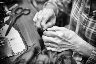 Yaşlı bir kadının eski bir dikiş makinesinin yanında giysi parçasıyla çalışması. Siyah ve beyaz tonda. Kıyafet değiştirme konsepti