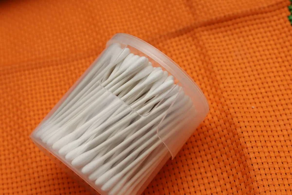 Cotton buds or cotton swabs in transparent plastic box on orange cloth