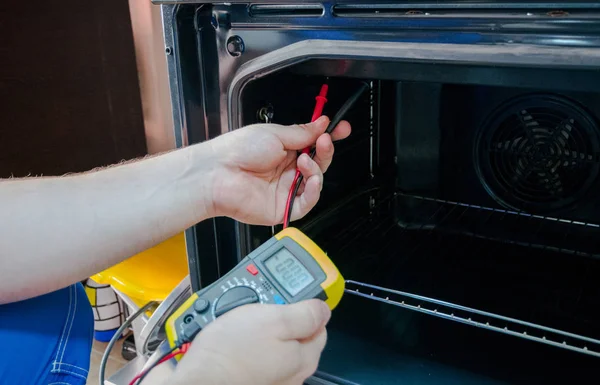 Young man with multimeter repairing oven, closeup