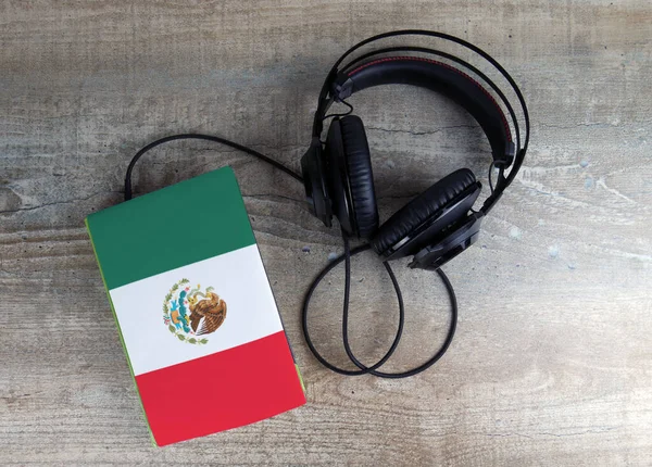Headphones and book. The book has a cover in the form of Mexico flag.