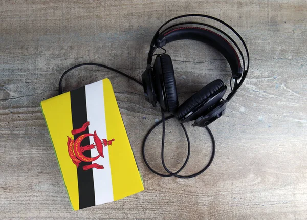 Headphones and book. The book has a cover in the form of Brunei flag.