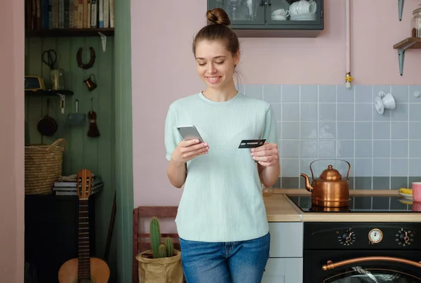 Pretty young woman buying goods and services with app store, paying on-line, spending electroinc money or digital currency from husband's bank account, ordering food