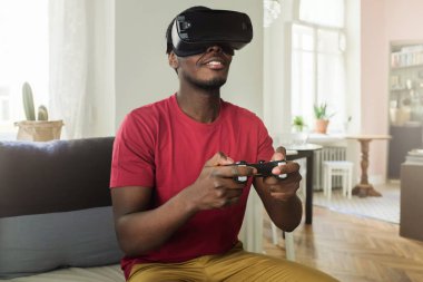 Afro-Amerikan delikanlı VR gözlük ve kablosuz joystick kullanarak, 360 derece sanal gerçeklik kulaklık çağdaş rahat iç Oyunlar için zevk oyun oynama