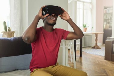 Kanepede kapalı yalnız oturan, Merhaba teknoloji akıllı vr gözlük ve kırmızı t-shirt giyiyor, 360 derece video izlerken heyecanlı genç Afro-Amerikan adam hayran