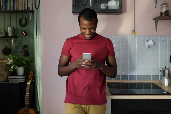 Joven Hombre Afroamericano Sonriente Sosteniendo Teléfono Inteligente Con Ambas Manos —  Fotos de Stock