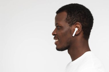 Müzik veya radyo, dinleme genç Afro-Amerikan erkek gülümseyen yana portresi boş beyaz t gömlek giymiş modern kablosuz kulaklık kullanır. Metin için yer kopyalayın