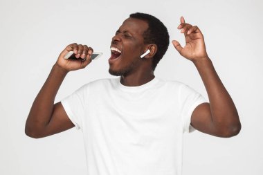 Boş beyaz t gömlek, gri arka plan üzerinde izole kapalı gözlerle onun en sevdiği şarkıyı genç Afro-Amerikan yakışıklı