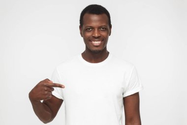 Gri arka plan üzerinde gülümseyen güzel Afrikalı-Amerikalı adam işaret parmağı, kopya alanı için reklam, ile onun boş beyaz t gömlek gösteren izole