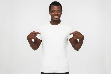 Gri arka plan üzerinde gülümseyen güzel Afrikalı-Amerikalı adam boş beyaz t-shirt kopya alanı için reklam, her iki işaret parmakları ile işaret izole