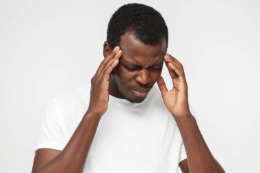 Huzursuz, duygu tapınaklar el ile dokunmak genç Afrikalı-Amerikalı adam boş beyaz t gömlek gri arka plan üzerinde duygu ağrı, izole yorgun ve hoşnutsuzluk
