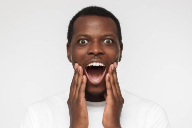 Atış yuvarlak gözler ve ağız, olumlu şok ile son derece şaşırttı seyir yakışıklı Afrikalı-Amerikalı gencin boş beyaz t gömlek, beyaz arka plan üzerinde izole kapatmak