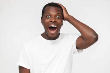 Headshot fotoğraf makinesi, büyük satış fiyatları ile şaşırmış gibi bakıyorsun boş Beyaz tişörtlü yakışıklı sürpriz Afro-Amerikan insanın elini başının üstüne gri arka planı tutarak