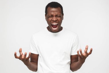 Gri backgroung karşı izole ayakta ve umutsuzca, iki elinizle işaret çığlık boş beyaz t shirt, Afro-Amerikan yakışıklı
