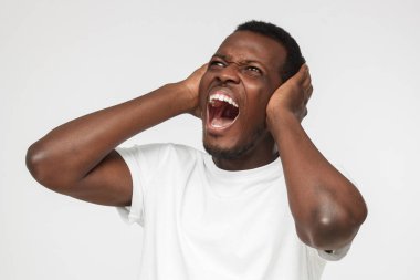 Boş beyaz t gömlek Not kulakları her iki el ile kapatma gürültü ile vurguladı gürültülü komşular, genç Afro-Amerikan adam önlemek dinleme mücadele