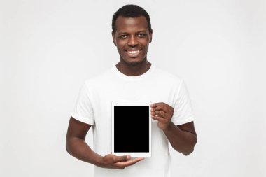 Genç Afrikalı-Amerikalı adam boş tablet ekran sunan bir gülümseme ile izleyiciler, boşaltmak için reklam mal veya apps üzerinde moda gözlük ile resimde izole üzerinde gri arka plan