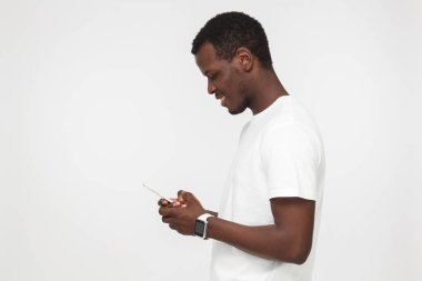 Yana doğru genç çekici Afro-Amerikan gülümseyen adam arıyor ve smartphone ile manifatura süre istimal hareket eden telefon, gri arka plan üzerinde izole arkadaşı vurdu