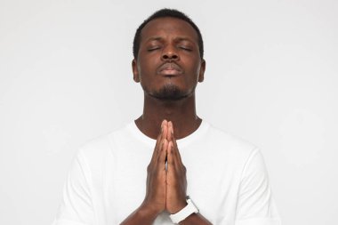 Stresli seyir gri arka plan üzerinde izole genç Afro-Amerikan adam ile dua ediyor sanki el araya koyarak depresyon üstesinden gelmek için gözler kapalı