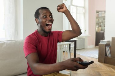 Bağırarak, tezahürat, gol kutluyor heyecanlı, duygu parlak kırmızı T-shirt izlerken spor maçında televizyon ve onun favori takım destekleyen bir Afrikalı-Amerikalı adam yatay fotoğraf giyinmiş