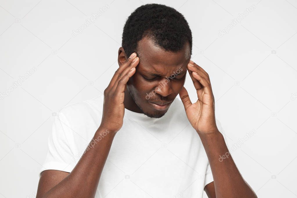 Young African American man in blank white t shirt isolated on gray background, feeling pain, touching temples with hands, feeling uneasy, tired and discontent