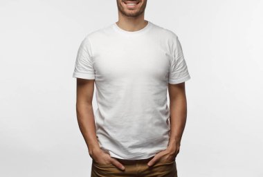 Elleri ceplerinde duran, logo veya metin, gri arka plan üzerinde izole kopya alanı olan boş beyaz tshirt giyen genç Avrupa adam