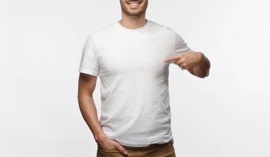 Reklam metin veya logo, gri arka plan üzerinde izole statning için boş alan gösterilen çekici genç adam onun boş beyaz tshirt işaret parmağı ile işaret eden şeffaf gözlük