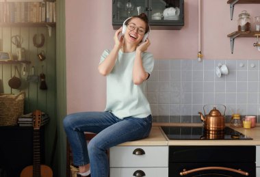 Taşıma ve onun oyuncu için olumlu ses parçalarını dinlediğini smiling boş vaktinizi dairesinde mutfak masasında bir parçası koltuk olarak kullanarak Avrupa beyaz bir kadın yatay çekim