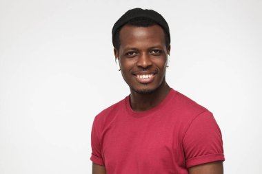 Kırmızı hipster T-shirt ve yeni beyaz radyo earphones ile yeni teknolojik fırsatları memnun gri arka plan üzerinde izole emin Afrikalı-Amerikalı gencin closeup headshot