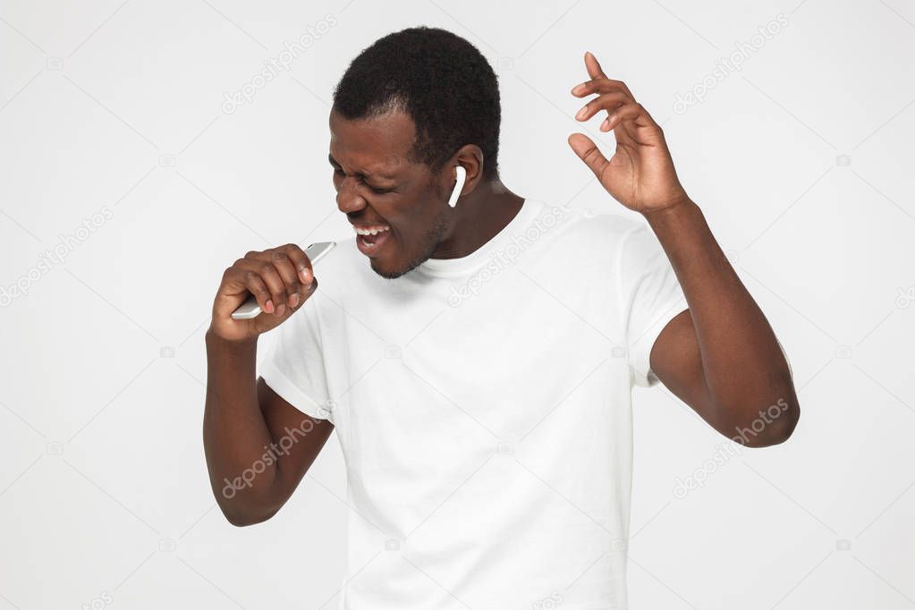 Indoor portrait of young handsome African man isolated on gray background having turned left during dance to playlist he is listening from cellphone through headphones without cord, being excited