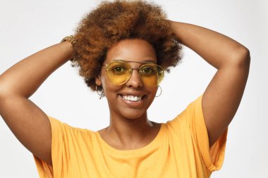 Paylaş fikir istekli gri arka plan, trendy gözlükler, rahat gösterilen giyen ve dostça gülümseme dişlek, izole genç gülümseyen koyu tenli Afrika kökenli Amerikalı kadın portresi stüdyo