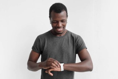 Dokunmatik ekranlı akıllı saatler kontrol kablosuz kulaklık ve gri t tişört giyen genç Afro-Amerikan adam