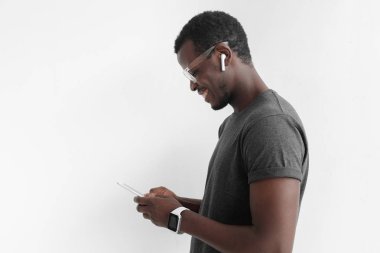 İleti değiş tokuşu veya Internet'te sörf yaparken akıllı telefon ekranına bakarak gri tişörtlü, gri arka plan üzerinde izole yakışıklı Afrikalı-Amerikalı adam portresi yan