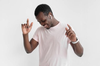 Genç yakışıklı Afrika adam kablosuz kulaklık ve onun en sevdiği şarkıyı dinlerken, dans doğal pembe t gömlek ile gülümseyen gözleri kapalı