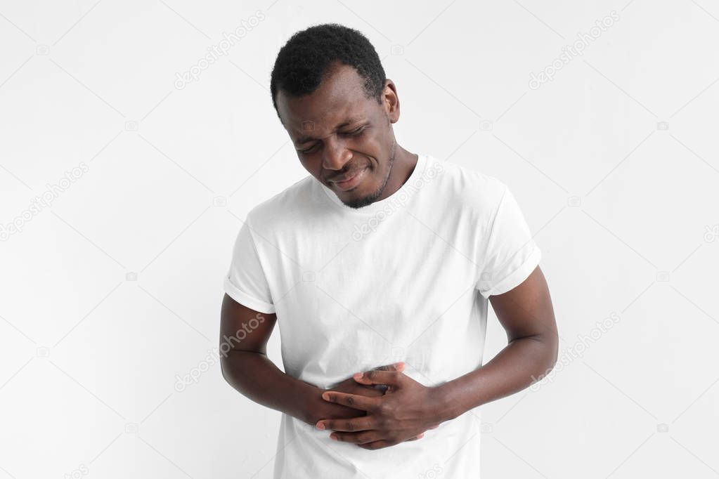 Upset unhappy young african american man holding his abdomen with both hands, suffering from bellyache