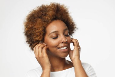 Genç esmer kız closeup headshot sesleri gülümseme ile beyaz radyo earphones parmak basarak kapalı gözlerle onun favori ses parçaları hareketli izole üzerinde gri arka plan resim