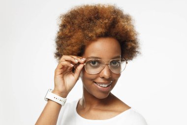 İzole üzerinde gri arka plan beyaz bluz giyen kol saati ve havacı gözlük, holding kenar olumlu gülümseyen parmaklarıyla, giyinmiş genç Afro-Amerikan Kız yatay fotoğraf resimde