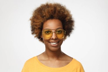 Parlak sarı üst ve giyen gözlük eşleşen renk, gülümseyen, arkadaşları ile eğlenmek için hazır closeup headshot Afrikalı-Amerikalı kadın gri arka planı izole ayakta giymiş