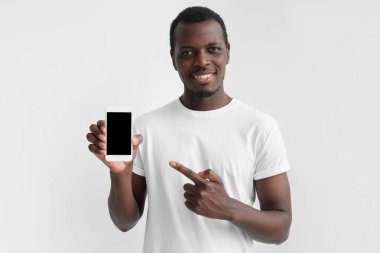 Genç Afrika yatay closeup resimde izole üzerinde gri arka boş smartphone bir elinde tutan adam ve parmak ile işaret reklam ürünleri ve hizmetleri için alan kopyalayın