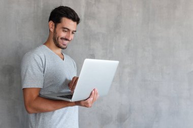 Web içerik paylaşımı kopya alanı ile dokulu gri duvara reklamlar için ayakta, dizüstü holding ve medya mutlu gülümseme ile izlerken genç yakışıklı adam