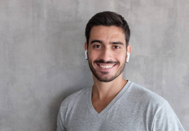Listeting gri dokulu duvar karşı ayakta onun favori müzik parçası için t gömlek giymiş genç gülümseyen yakışıklı adam headshot kapatmak