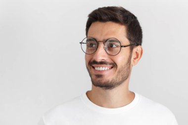 Yakışıklı genç Avrupa beyaz adam gri arka plan üzerinde izole kapalı portresi giyinmiş bir kenara seyir bir şey eğer döndü yuvarlak gözlük, casual beyaz tişört içinde