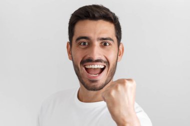 Gün ışığından yararlanma tutkulu genç gülümseyen gülen ve takım destekleyen veya rekabet zaferini kutluyor heyecan içinde rahat t-shirt giyen gri arka plan üzerinde izole portresi