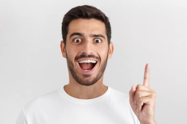 Ağzı açık, işaret parmağını eureka t-shirt, büyük yenilik düşünce, sahip kayıt beyaz genç gülümseyen yakışıklı portresi kapatın